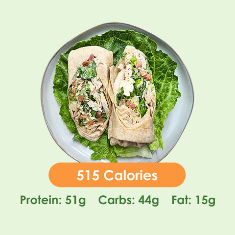 Two halves of a generously filled chicken caesar wrap, showcasing crisp lettuce and savory chicken, served on a bed of fresh greens.