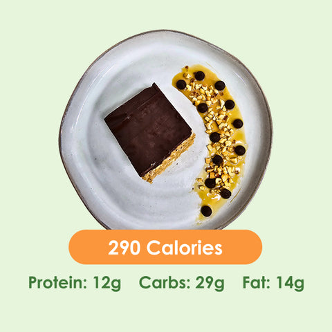 A delicious Fit Snick bar with a chocolate top, served on a plate with a drizzle of caramel, chocolate chips, and chopped nuts.